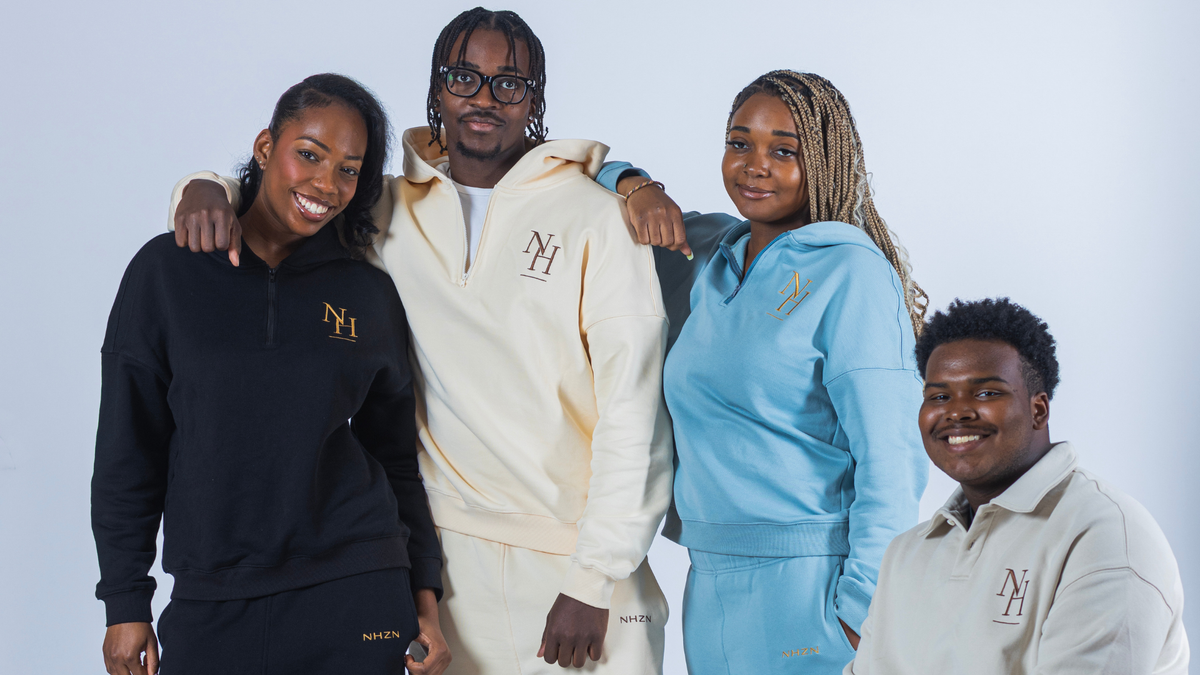 Four people wearing matching custom tracksuits with a gold 'NH' logo, posed together against a light gray studio background. The tracksuits include black, cream, light blue, and light gray colorways.